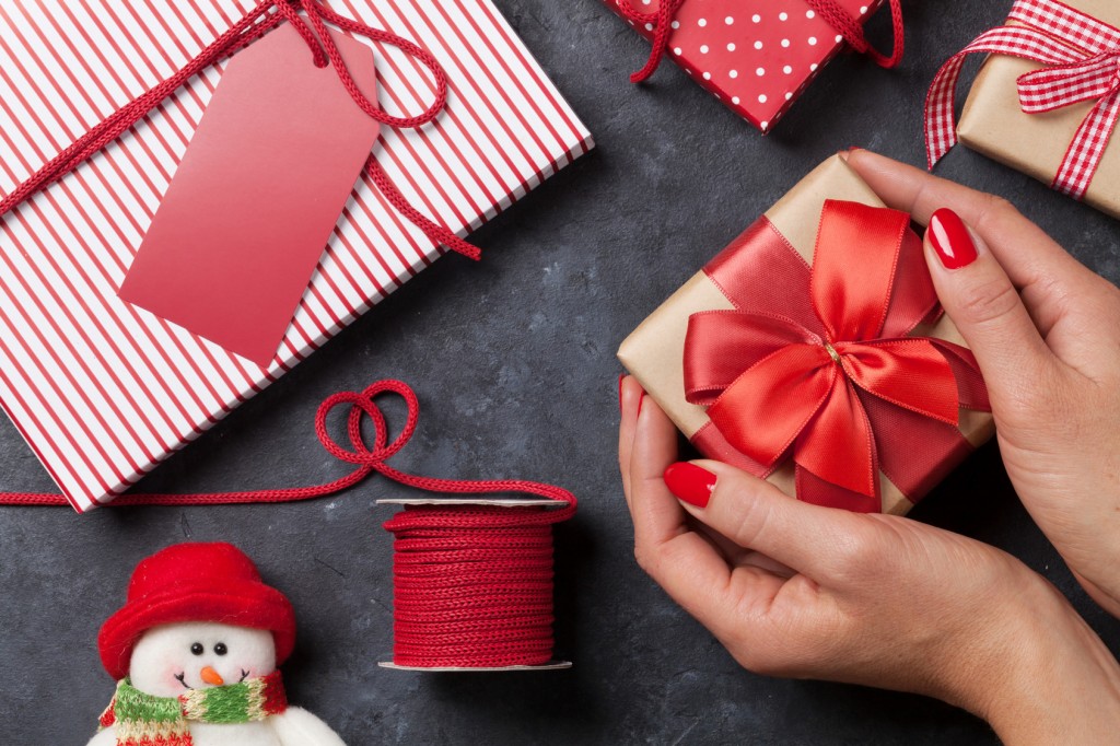 Female hands holding christmas gift above stone table. Top view. Xmas gift wrapping